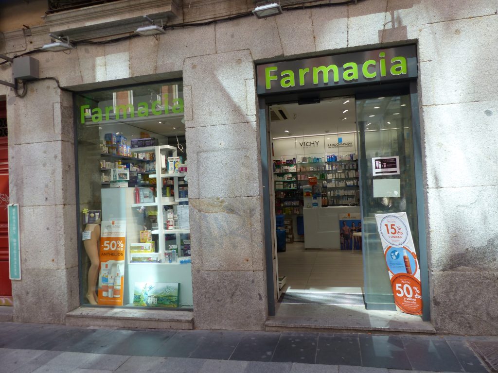 Fachada de una farmacia con el cartel verde iluminado y escaparate